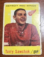 Front of vintage 1959-60 Topps trading card showing color photo of Terry Sawchuk in Detroit Red Wings red uniform with team logo, yellow background and name text.