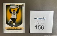 Front of the Sidney Crosby hockey card showing player lifting the Stanley Cup trophy with gold and black design elements.