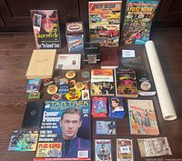 Full display of assorted collectible items on floor including books, trading cards, magazines, pinback buttons, currency, and a rolled map.