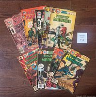 Photo of the 9 Charlton Fighting Marines comics arranged on floor with lot number card visible.