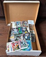 Open box showing a large pile of football cards inside a cardboard box with cards stacked and scattered, displaying various player images and card fronts.