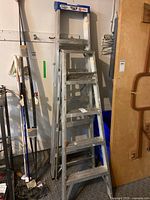 Two aluminum ladders standing in garage, one taller straight ladder and one shorter A-frame step ladder.