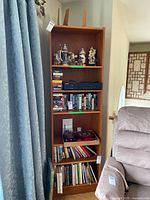 Full view of the bookcase showing the overall structure and the display of items on all shelves near a curtain and armchair.