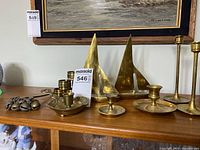 Photo showing six brass items on wooden surface: two tall candlesticks, two shorter candlesticks with attached trays, and two sailboat figurines.
