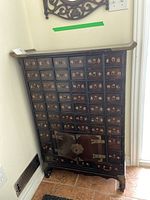 Front view of dark brown wood apothecary cabinet with multiple small drawers and cabinet doors.