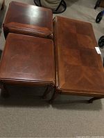 Photo showing stack of four square wooden end tables next to a single coffee table, highlighting finish and shape similarities.