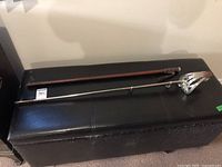 Full length of sword laid alongside brown leather scabbard on black bench