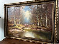 Frontal view of the full painting showing the framed forest landscape with water reflection.