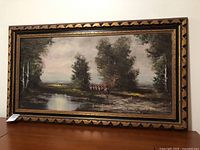 Full view of the framed landscape painting featuring trees, water, and figures on horseback.