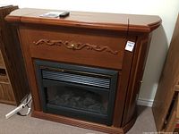 Full view of wooden electric fireplace showing decorative carved front and glass window with faux flame effect.