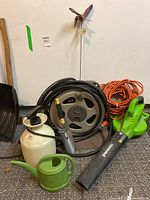 Overview of all items: garden hose on reel, hand sprayer, extension cord, watering can, trowel, and Greenworks blower.