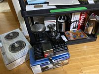 Overview of kitchen appliances on floor and shelf including portable electric stove, Waring knife sharpener, Lagostina meat grinder, toaster, blender box, trays, and thermos.
