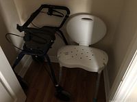 Walker and shower chair positioned in a corner on hardwood floor.