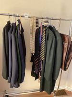 Multiple men's formal suit coats, military-style coat, neckties, fabric belts/straps, and two leather bags on a clothing rack