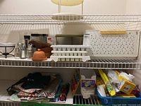 Shelf showing clay baker, ice cube trays, bread box with floral pattern, wooden bowls, salt and pepper shakers, canisters, and food wrap boxes