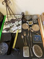 Overview image showing all items on a table with black surface, including metal picture stand, various silver plated utensils and dishes, cast animal figurines, and candle holder.