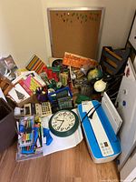 Overview photo showing majority of office supplies including corkboard, clock, printer, globe, and stationery