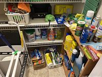 Wide view of shelving with multiple cleaning product bottles, sprays, powders, sponges, boxes, and rags.
