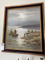 Framed oil painting of a sea scene with boats and rocky shore, showing full artwork and frame.