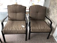 Pair of metal arm chairs with brown cushions placed side by side. Visible black metal frames and brown textured fabric cushions with tufting.