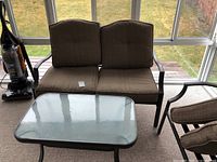 Patio loveseat with two brown cushions and matching rectangular glass top coffee table taken in sunroom.