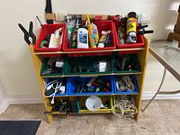 Front view of wooden shelving unit with multicolored bucket organizers containing wires, hand tools, and chemical bottles.