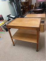 Full view of teak side table showing top surface, lower shelf, legs with casters, and surrounding environment.