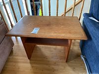 Full view of the teak side table positioned between furniture and railing, showing its overall shape and condition.