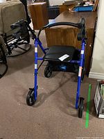 Front view of a blue four-wheel walker with a black seat placed indoors.