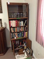 Front view of wooden wall unit with glass upper shelves, middle bookshelves filled with books, and lower closed cabinet with doors.