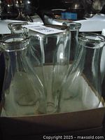 Top view of five clear glass milk bottles shown in a cardboard carrier with visible chips and dirt inside the bottles.
