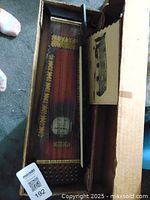 Top view of the violin-uke in box showing its wooden body, strings, and decorative markings.