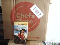 Photo of Harlequin Super Romance paperback book No Hero Like Him in front of a Chefs Plate box with a MaxSold lot sticker
