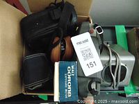 Box containing multiple vintage cameras, camera cases, and photography equipment including exposure meter and projector.
