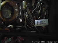 Cardboard box containing tarnished silver flatware (forks, spoons, knives) and decorative silver plate.