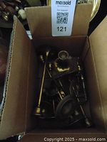 Box showing multiple brass pieces including candle sticks, jug, and goblets, viewed from top.