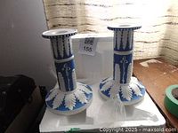 Pair of blue and white porcelain candle holders decorated with white leaf and floral relief designs, placed on a white surface.