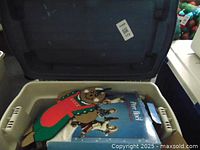 Open plastic tote showing boxed Pere Noel figurines and fabric gingerbread man decoration inside.