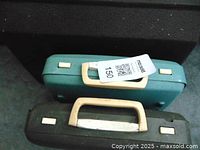 Two electric typewriters with plastic carrying cases, teal and dark green colors, stacked with labels.