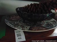 Photo showing the large pinecone inside the dark scalloped-edge glass fruit bowl sitting on the Japanese design platter