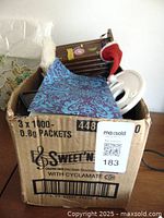 View into cardboard box filled with various decorative and miscellaneous items including a small outhouse, Santa hat, and patterned cloth