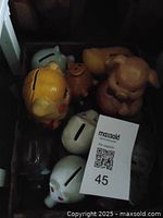 Photo showing seven piggy banks of various shapes including dogs, pigs, bears, and glass material in different colors such as yellow, white, brown, and clear glass. Some show visible wear and cracks.