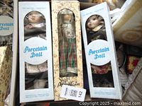 Several boxed porcelain dolls including one in a plaid skirt, arranged side by side.