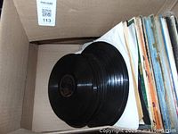 Box containing a stack of 78 RPM vinyl records without sleeves, black discs visible.