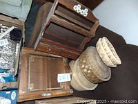 Two wooden spice racks placed on a couch with woven baskets next to them. One spice rack is open with two drawers, the other has a front door, plus multiple natural fiber baskets in various sizes, some with lids.