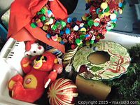 Photo showing plush Christmas bird ornaments, sequin wreath, ceramic holly plate, and striped ornament ball inside plastic tote.
