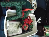 Top-angle view of a plastic tote containing an artificial Christmas reindeer figure, poinsettia flowers, holiday gift bag, and framed Christmas photo.