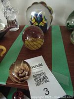 Photo showing three vintage glass paperweights including a rose design, butterfly motif inside clear glass, and gold swirl spherical paperweight on wood surface.