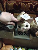 Front view showing face of piggy bank with ceramic rose and leaf decoration and coin slot on top.