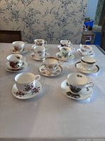 Eleven assorted teacup and saucer sets arranged on table, each with distinct floral designs and gold accents.